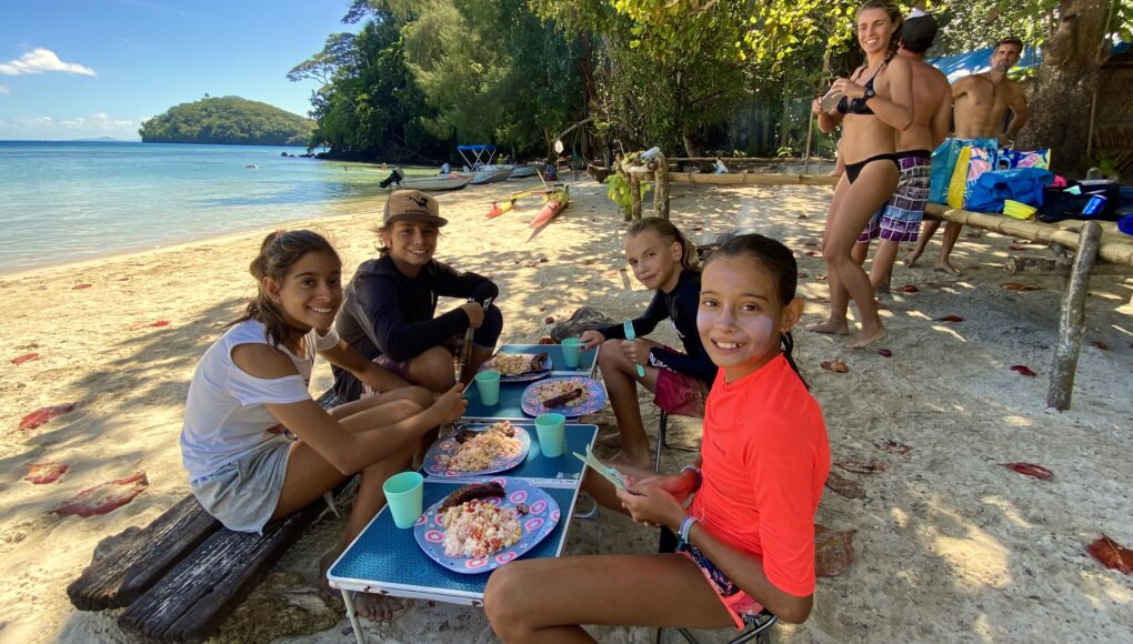 A smiling family on the the beach enjoying a bbq in a turquoise lagoon